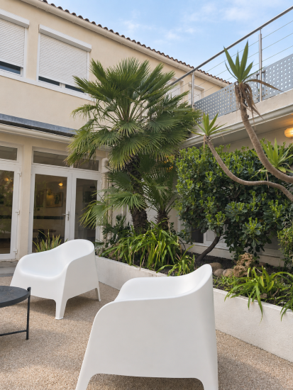 Patio de l’hôtel à Châtelaillon-Plage avec fauteuils blancs, palmier et jardin tropical