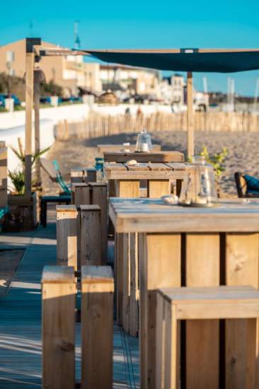 Terrasse du bar de plage avec tables hautes et tabourets en bois face à la mer